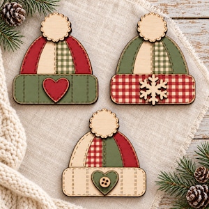 May include: Three wooden hat-shaped ornaments featuring pom-poms. One hat is red and green with a heart, one is green and red with a snowflake, and one is cream and red with a heart and button. Each piece has a flat, layered design.