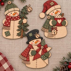 May include: Three wooden snowman ornaments with painted details. One holds a green tree with a bell, one holds a red mug with a heart and a bell, and one holds a large star with a red bow. Each snowman wears a hat and scarf with buttons.
