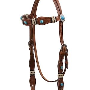 Può includere: Una briglia da cavallo in pelle marrone con accenti turchesi. La briglia presenta cuciture decorative, pietre color turchese e un concho color argento. Il design include accenti intrecciati bianchi e neri. La briglia è progettata per l'equitazione.