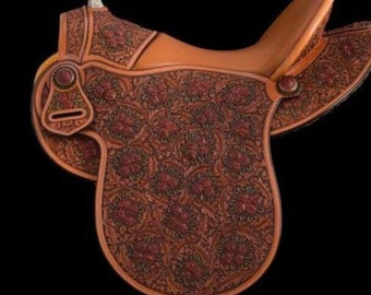 Könnte beinhalten: Ein brauner Ledersattel mit aufwendigen floralen Verzierungen. Der Sattel hat einen hohen Hinterzwiesel und einen silbernen Horn.