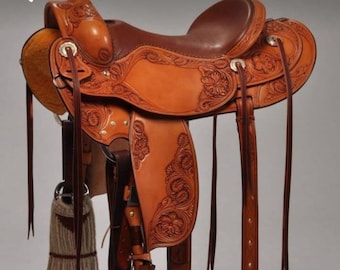 May include: A brown leather saddle with intricate floral carvings. The saddle has a high cantle and a deep seat. The stirrups are made of metal and have leather straps.