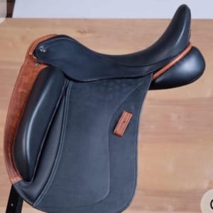 以下が含まれることがあります： 黒と茶色の革製イングリッシュサドル。サドルは、濃い色の座面、ニーパッド、フラップを備え、側面には明るい茶色の革のアクセント、木製のあぶみが付いています。 このサドルは乗馬用に設計されています。