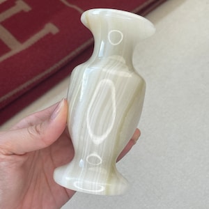 Op de afbeelding: Een kleine, witte marmeren vaas met een delicaat, elegant ontwerp. De vaas heeft een gladde, gepolijste afwerking en een licht uitlopende opening.