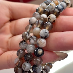 Puede incluir: Un brazalete de múltiples hilos hecho con cuentas de ágata grises y blancas. Las cuentas son redondas y tienen un acabado natural y pulido.