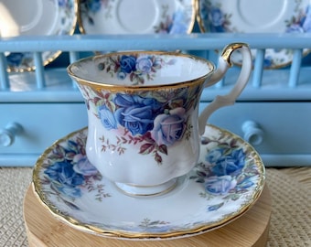 Peut inclure: Une tasse à thé et une soucoupe blanches avec un motif floral bleu et or. La tasse et la soucoupe sont sur un support en bois.