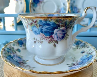 May include: A white teacup and saucer with a blue and pink floral pattern. The cup and saucer have a gold trim.