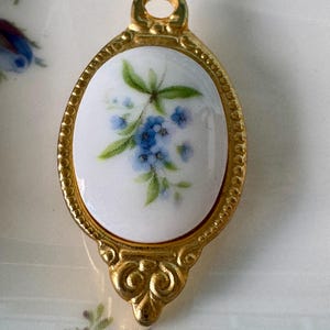 May include: A gold-toned spoon with a white porcelain oval handle featuring a blue and green floral design.