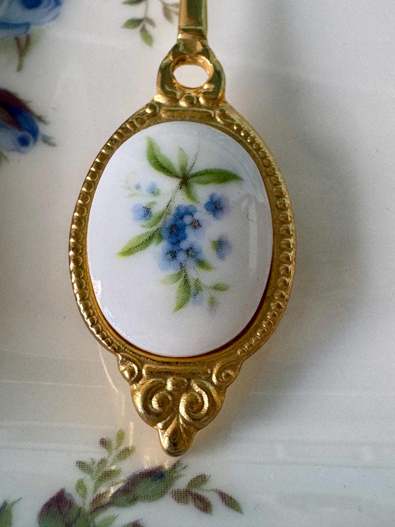 May include: A gold-toned spoon with a white porcelain oval handle featuring a blue and green floral design.