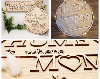 Puede incluir: Tres letreros de madera con el texto "Home is where Mom is" en cada uno. Los letreros están hechos de madera marrón claro y tienen un aspecto rústico. Los letreros están decorados con un corazón y una pluma.