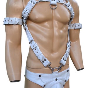 May include: White leather harness with adjustable straps, metal hardware, and a matching brief. The harness features a chest strap, shoulder straps, and arm cuffs. The design includes a ring at the chest and a jockstrap-style bottom.