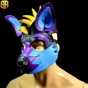 May include: A black, purple, and blue leather mask with a dog-like snout and ears. The mask has a yellow accent on the top of the head and a silver ring on the nose.