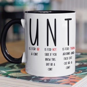 May include: White coffee mug with a black rim and handle. The mug has the word "UNT" printed in black letters. Below the word, there is a description of what each letter stands for.