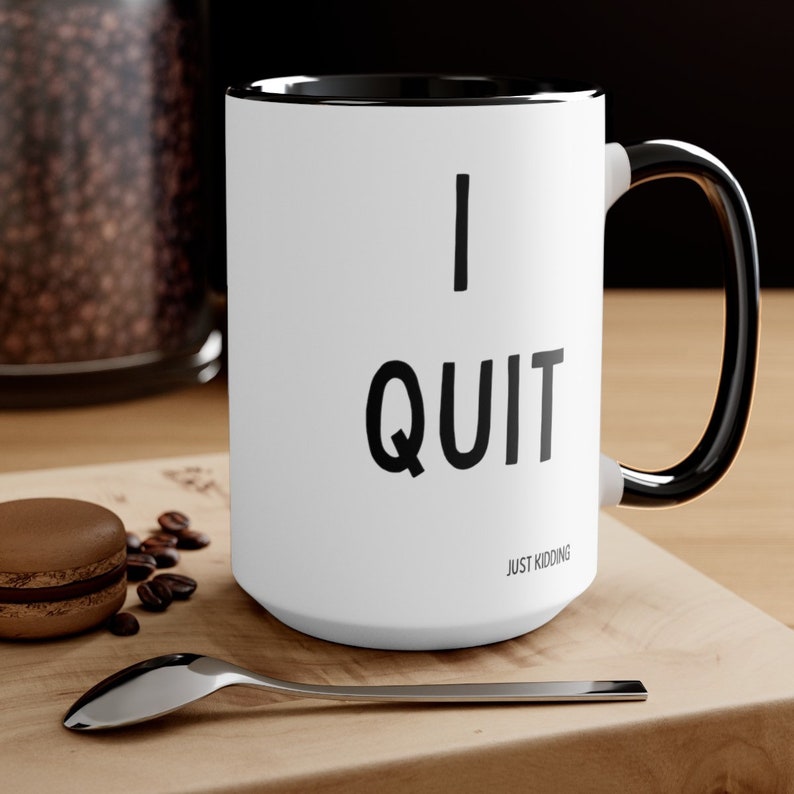 May include: White ceramic coffee mug with a black rim and handle. The mug has black text that reads "I QUIT JUST KIDDING".