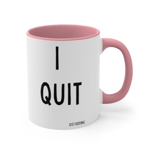 May include: White ceramic mug with a pink rim and handle. The mug has black text that reads "I QUIT JUST KIDDING".