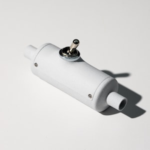 May include: A white cylindrical object with a silver toggle switch on top. The object has a textured surface and a small hole on the side.