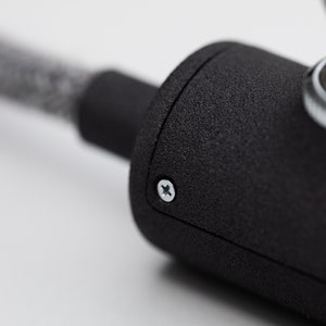 Watch close up of the switch light.The grey texture wire is going trough the inline switch case. The focus in on the  mate dark grey 3D printed switch case and the shiny screw.In the right top conner the toggle switch with the nut reflects the light.
