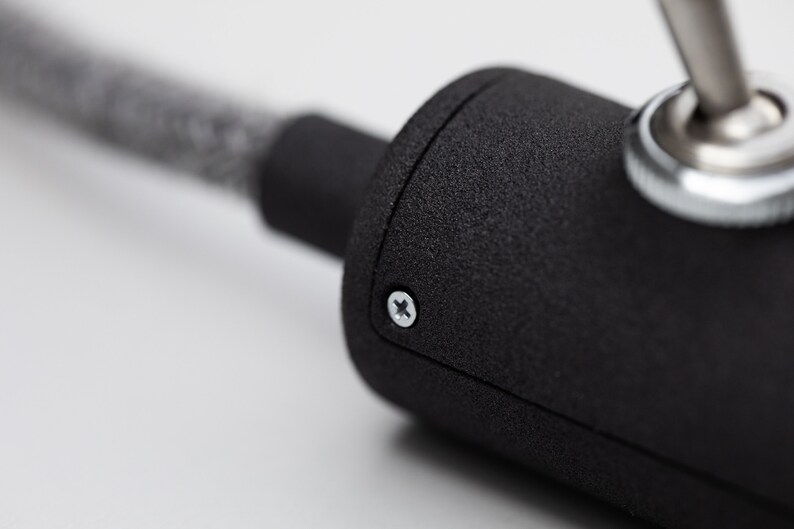 Watch close up of the switch light.The grey texture wire is going trough the inline switch case. The focus in on the  mate dark grey 3D printed switch case and the shiny screw.In the right top conner the toggle switch with the nut reflects the light.