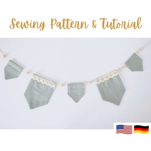 May include: A light green fabric garland with a white lace trim and wooden beads. The garland is hanging on a white wall. The text "Sewing Pattern & Tutorial" is at the top of the image. The American and German flags are at the bottom of the image.