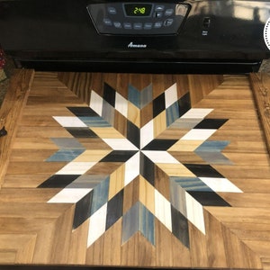 May include: A wooden serving tray with a starburst design in shades of blue, white, black, and brown. The tray has two black metal handles on the sides.