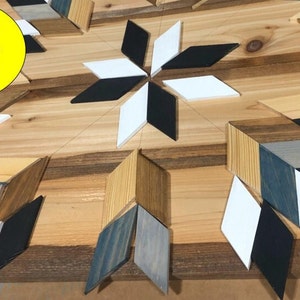 May include: Close-up of a wooden wall art piece with a geometric design. The piece is made of various wood pieces, painted in black, white, and shades of blue and brown. The text "Each board is hand painted and stained. Every piece is individually cut and glued into place." is visible in the image.