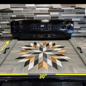 May include: A wooden stovetop cover with a geometric starburst design in shades of gray, black, white, and brown. The cover measures 30 inches by 22 inches.