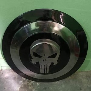 May include: A black and silver round shield with a white skull and crossbones design in the center.