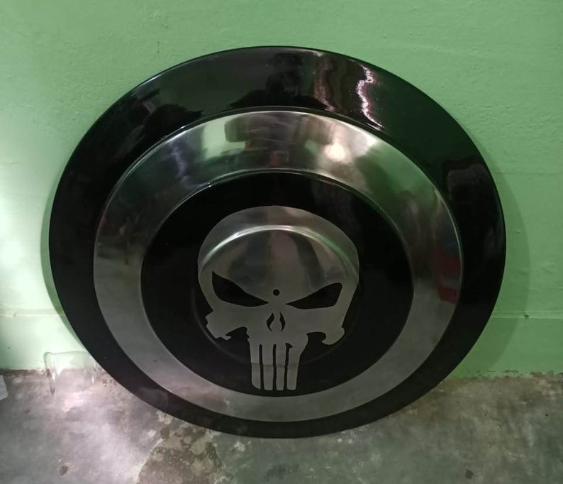 May include: A black and silver round shield with a white skull and crossbones design in the center.
