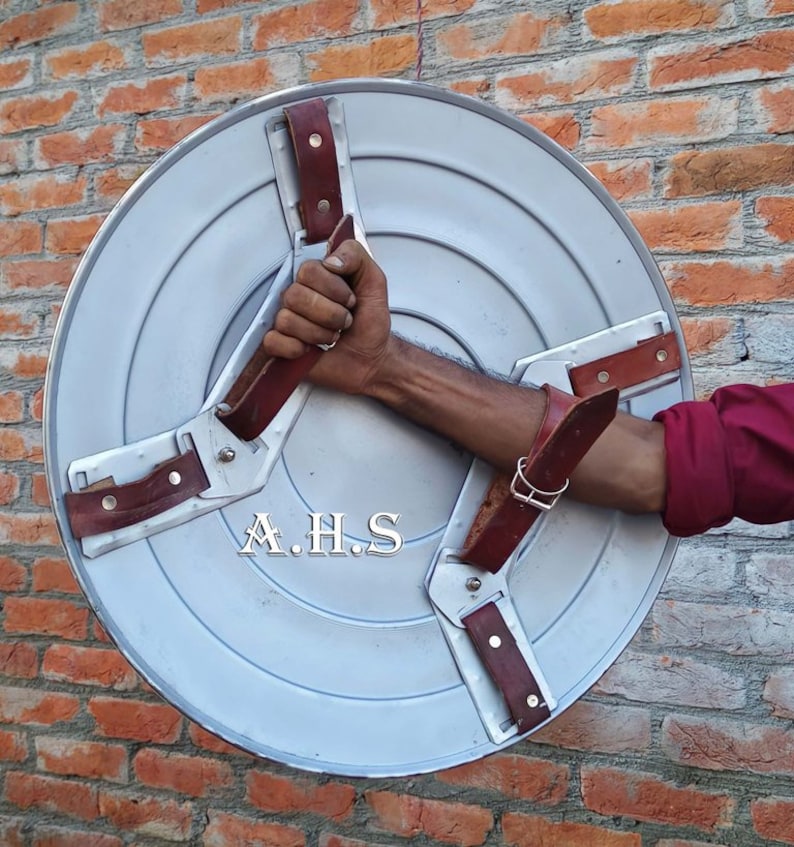 Peut inclure: Un bouclier en m&eacute;tal argent&eacute; avec trois lani&egrave;res en cuir marron. Le bouclier porte l'inscription "A.H.S.".