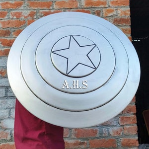 Peut inclure: Un bouclier Captain America de couleur argent avec une &eacute;toile noire au centre et les lettres A.H.S. imprim&eacute;es sous l'&eacute;toile.