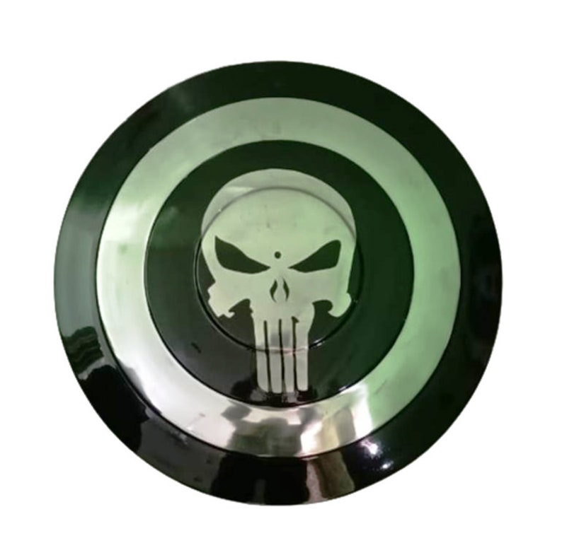 May include: A black and silver round shield with a white skull and crossbones graphic in the center. The skull has a small dot in the center of the forehead.