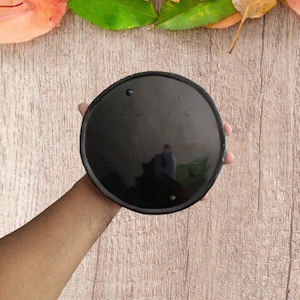 Könnte beinhalten: Ein kreisförmiger, einfarbig schwarzer Untersetzer mit einer glatten, glänzenden Oberfläche. Das Objekt hat ein schlichtes, flaches Design mit einer gleichmäßig dunklen Oberfläche und bietet ein sauberes, reflektierendes Erscheinungsbild.