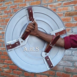 Peut inclure: Un bouclier en m&eacute;tal argent&eacute; avec trois lani&egrave;res en cuir marron. Le bouclier porte l'inscription "A.H.S.".