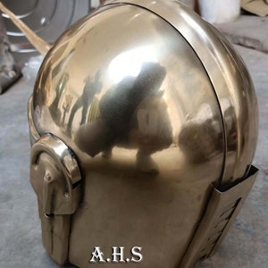 May include: A polished brass helmet with a rounded top and a detailed face guard. The helmet has a reflective surface, and the initials "A.H.S" are visible on the lower front. The design suggests a historical or fantasy theme.