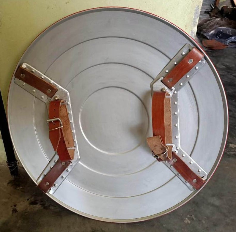 May include: A silver metal shield with a red and white star design. The shield has two brown leather straps with metal buckles.