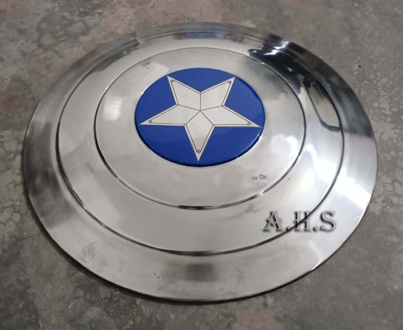 Pu&ograve; includere: Uno scudo di Captain America in metallo argentato con una stella blu e bianca al centro. Lo scudo ha un bordo rialzato ed &egrave; leggermente ammaccato. Il testo "A.H.S." &egrave; visibile in basso a destra dello scudo.
