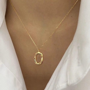 May include: A gold chain necklace with a simple, oval-shaped pendant. The pendant has a textured, organic look.