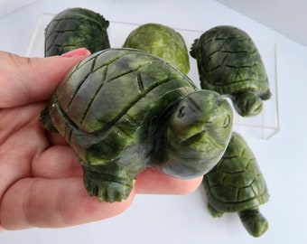 May include: Five green jade turtle sculptures, carved in detail, with a hand holding one of the turtles.