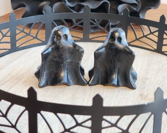 Peut inclure: Deux figurines de fantômes noires avec un design fantaisiste et effrayant. Les fantômes sont posés sur un plateau en métal noir avec un motif de toile d'araignée.