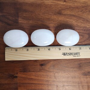 K&ouml;nnte beinhalten: Drei wei&szlig;e, oval geformte Steine, jeder etwa 5 cm lang, sind auf einer Holzoberfl&auml;che aufgereiht. Ein Lineal ist unter den Steinen platziert, mit den Zahlen 1 bis 8 sichtbar.