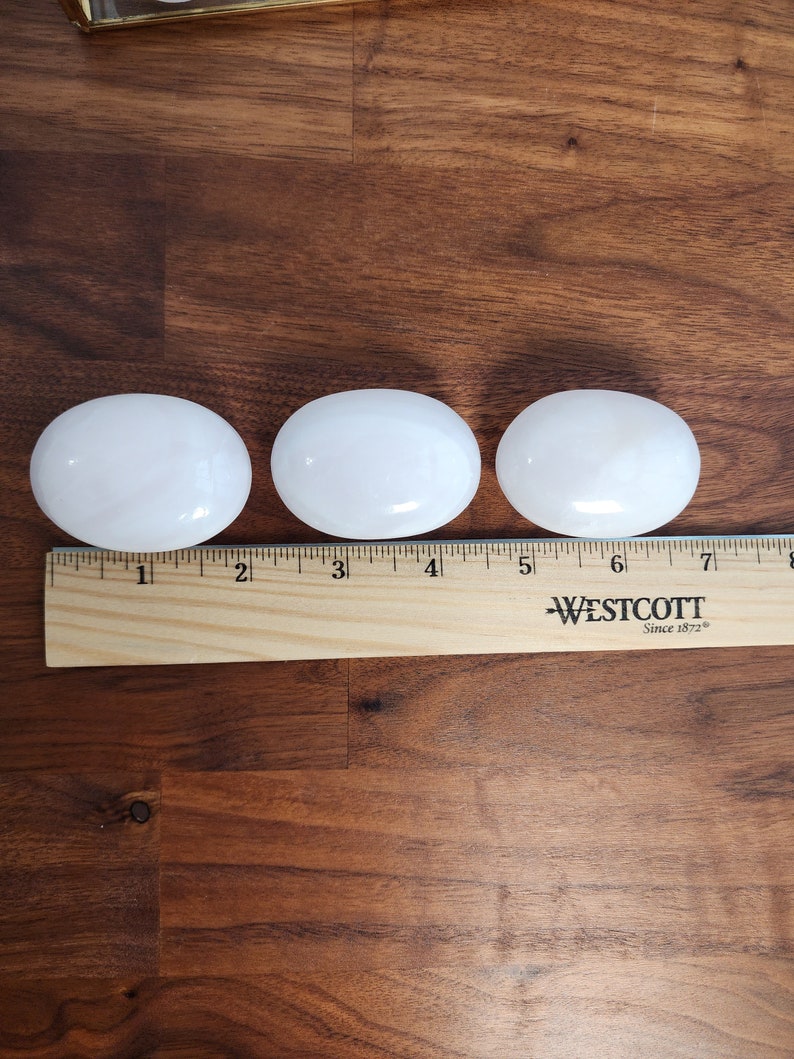 K&ouml;nnte beinhalten: Drei wei&szlig;e, oval geformte Steine, jeder etwa 5 cm lang, sind auf einer Holzoberfl&auml;che aufgereiht. Ein Lineal ist unter den Steinen platziert, mit den Zahlen 1 bis 8 sichtbar.