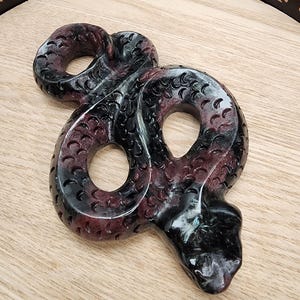 May include: A black and purple resin snake figurine with a detailed, textured surface. The snake is curled in a figure eight shape.