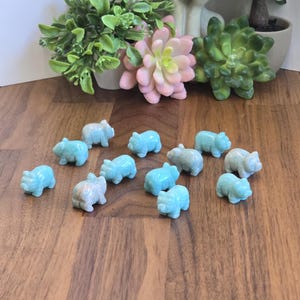 May include: A collection of thirteen small, hand-carved figurines shaped like pigs, crafted from a smooth, light blue stone with subtle white marbling. Each piglet is depicted in a standing position, showcasing a polished finish and uniform size.