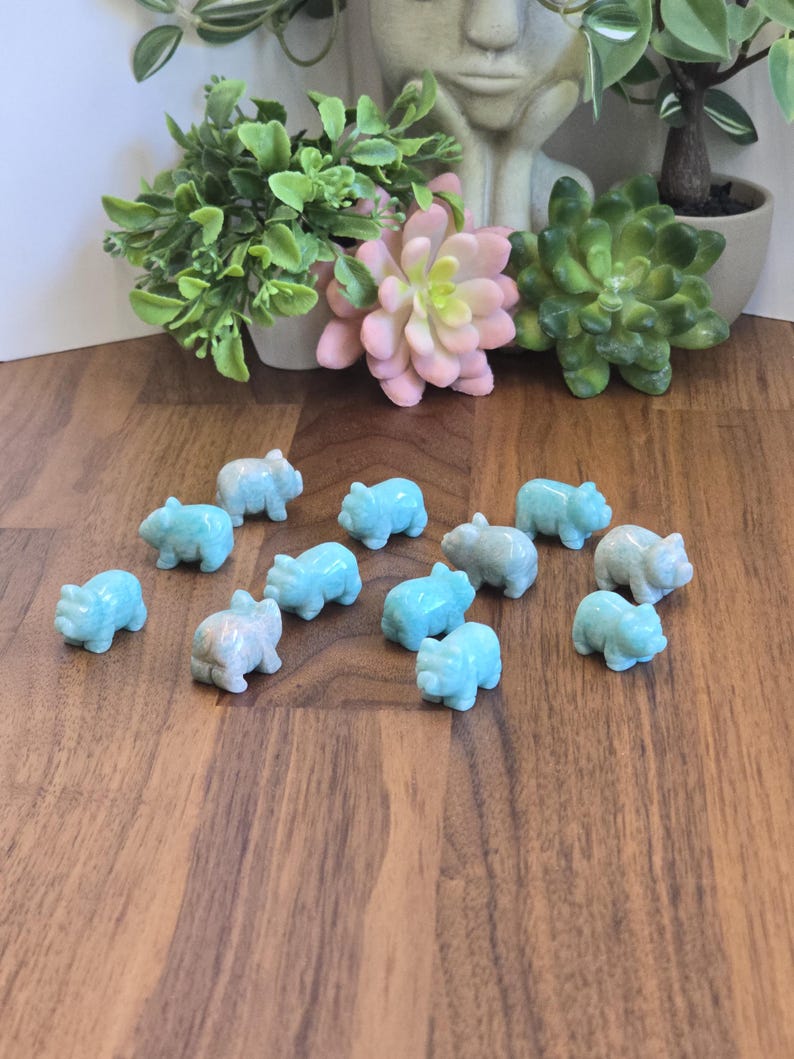 May include: A collection of thirteen small, hand-carved figurines shaped like pigs, crafted from a smooth, light blue stone with subtle white marbling. Each piglet is depicted in a standing position, showcasing a polished finish and uniform size.