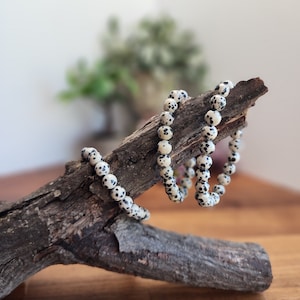 May include: A white and black speckled stone bracelet on a piece of driftwood.