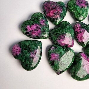 May include: A group of eight heart-shaped green and pink gemstones. The stones are polished and have a smooth, shiny surface.