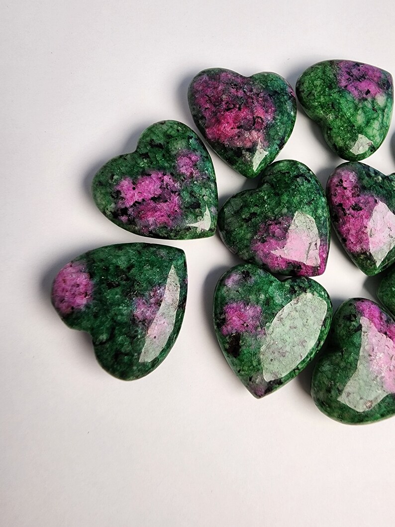 May include: A group of eight heart-shaped green and pink gemstones. The stones are polished and have a smooth, shiny surface.