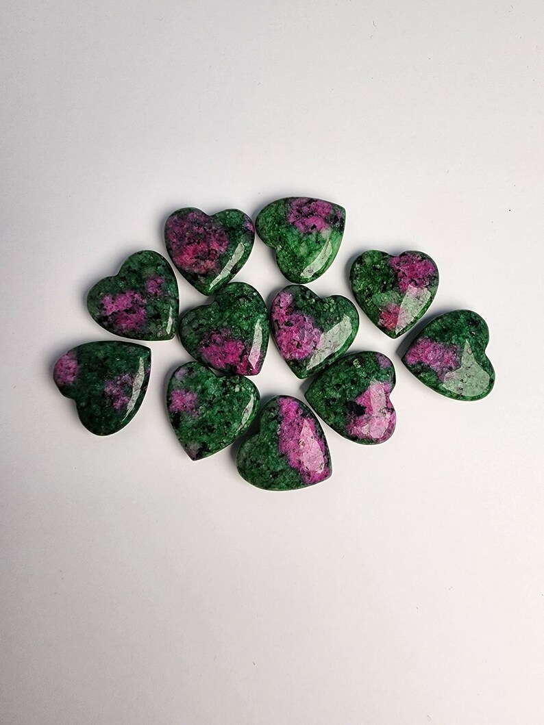 May include: A collection of ten heart-shaped green and pink gemstones. The stones are polished and have a smooth, glossy finish.