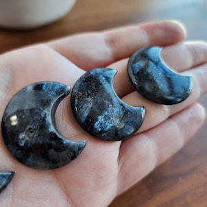 May include: Three black and blue crescent moon shaped stones. The stones have a sparkly, iridescent finish.