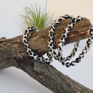 May include: A strand of black and white agate beads wrapped around a piece of driftwood. The beads are round and have a polished finish.