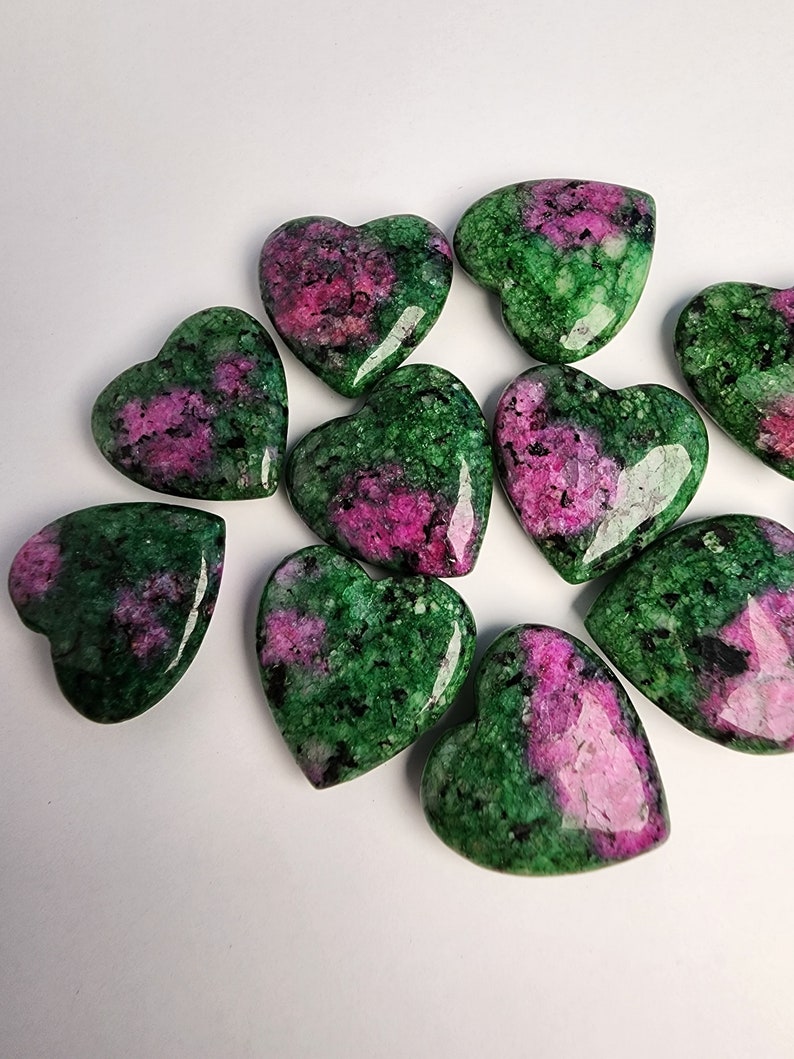 May include: A collection of ten heart-shaped green and pink gemstones. The stones are polished and have a smooth, glossy finish.